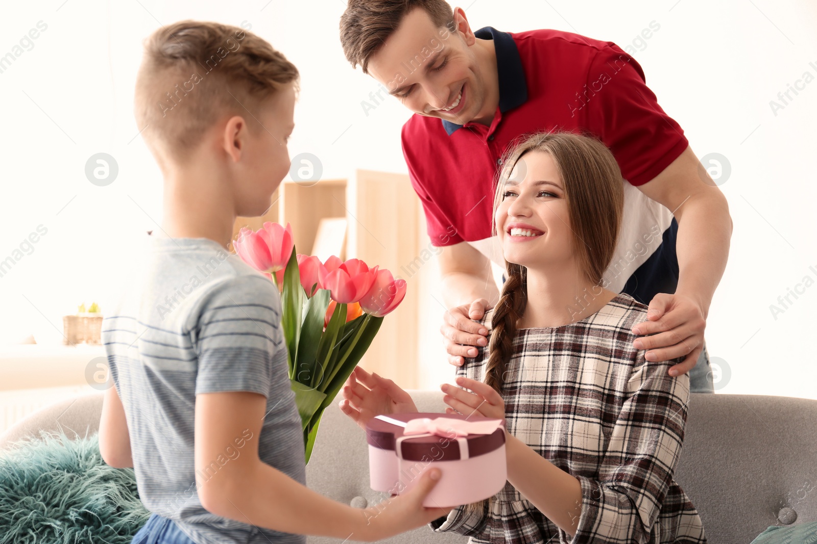 Photo of Happy woman receiving flowers and gift from her family at home. Mother's day celebration