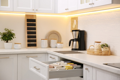 Open drawer with cups and coffeemaker on countertop in kitchen