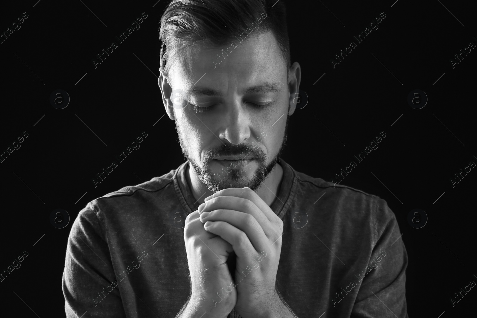 Photo of Man with hands clasped together for prayer on dark background, black and white effect