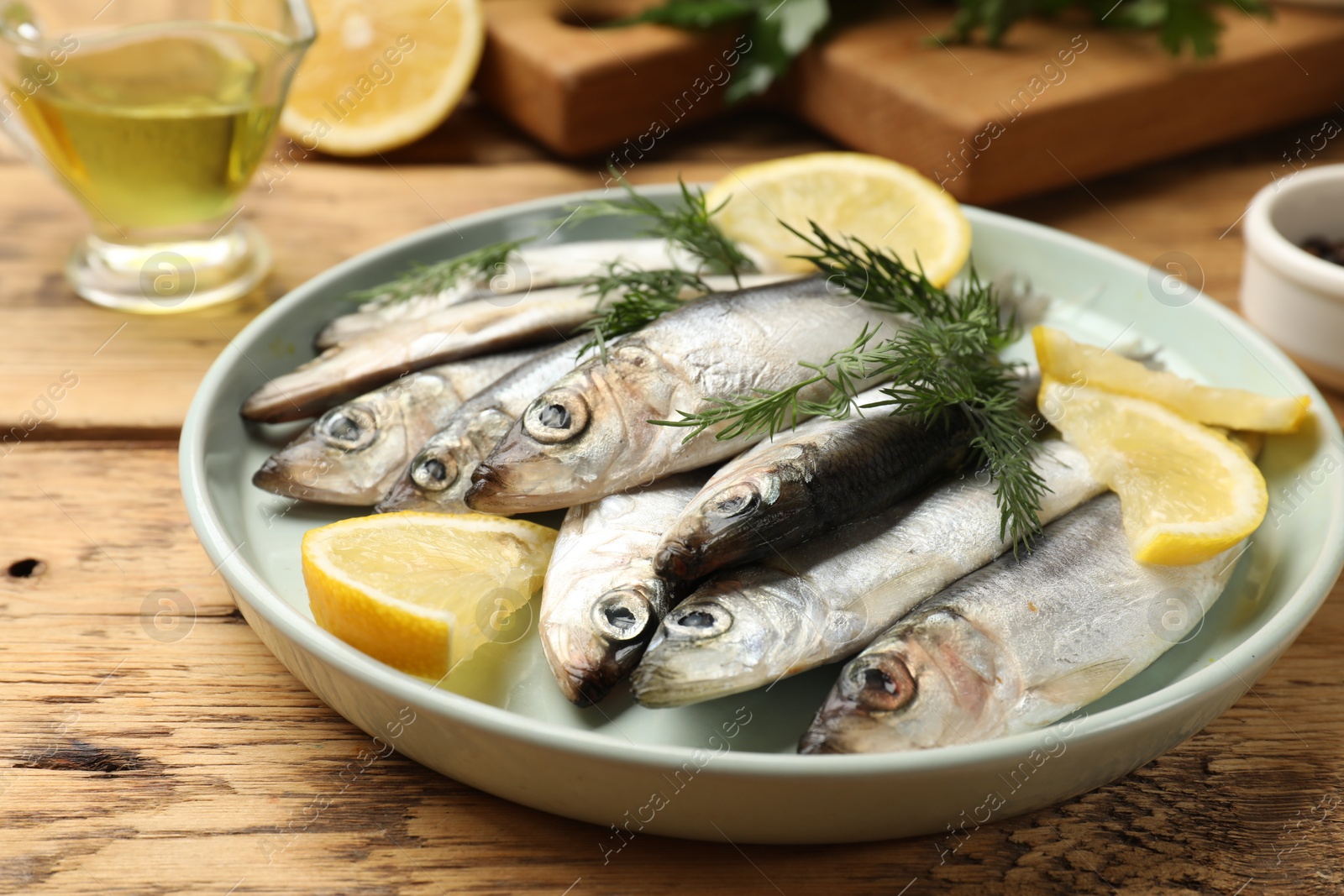 Photo of Fresh raw sprats, lemon and dill on wooden table, closeup