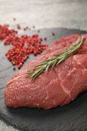 Photo of Piece of raw beef meat, rosemary and red peppercorns on table, closeup