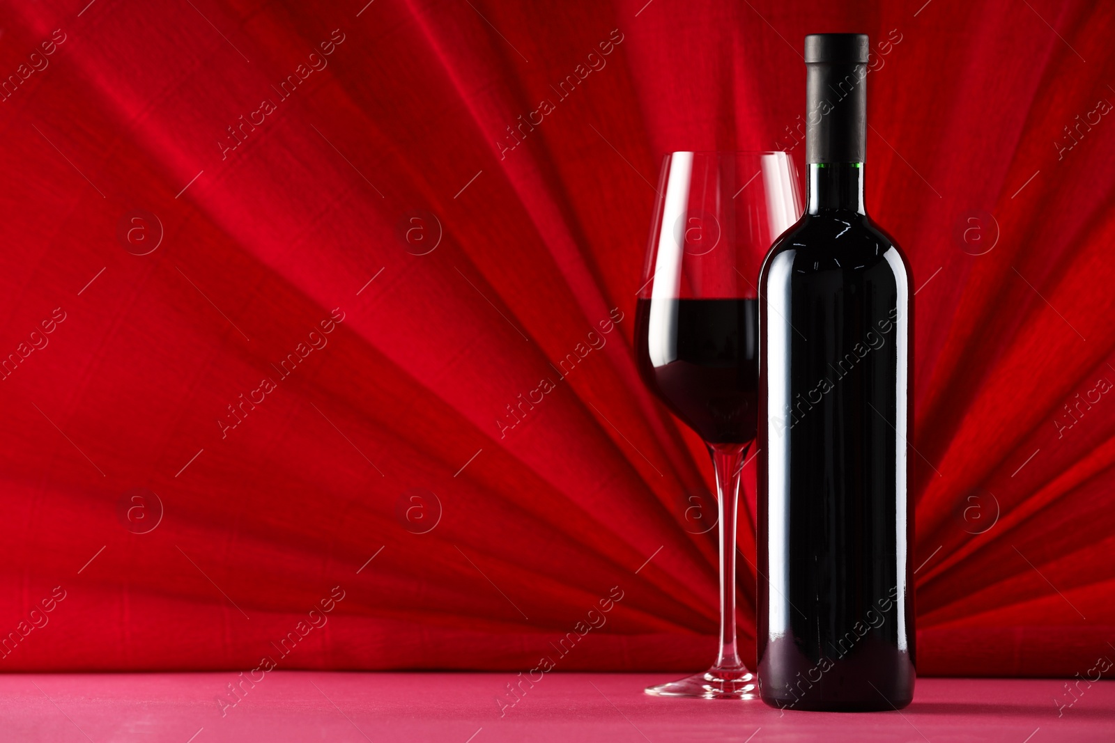 Photo of Stylish presentation of delicious red wine in bottle and glass on color background. Space for text