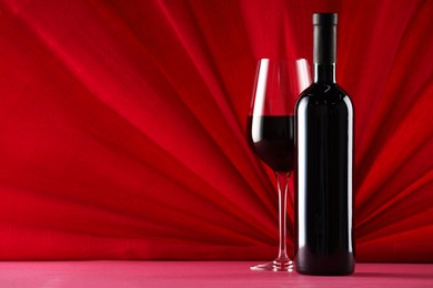 Stylish presentation of delicious red wine in bottle and glass on color background. Space for text