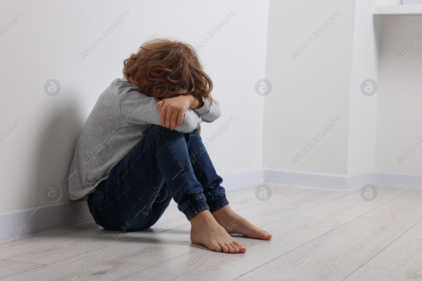 Photo of Child abuse. Upset boy sitting on floor near white wall, space for text