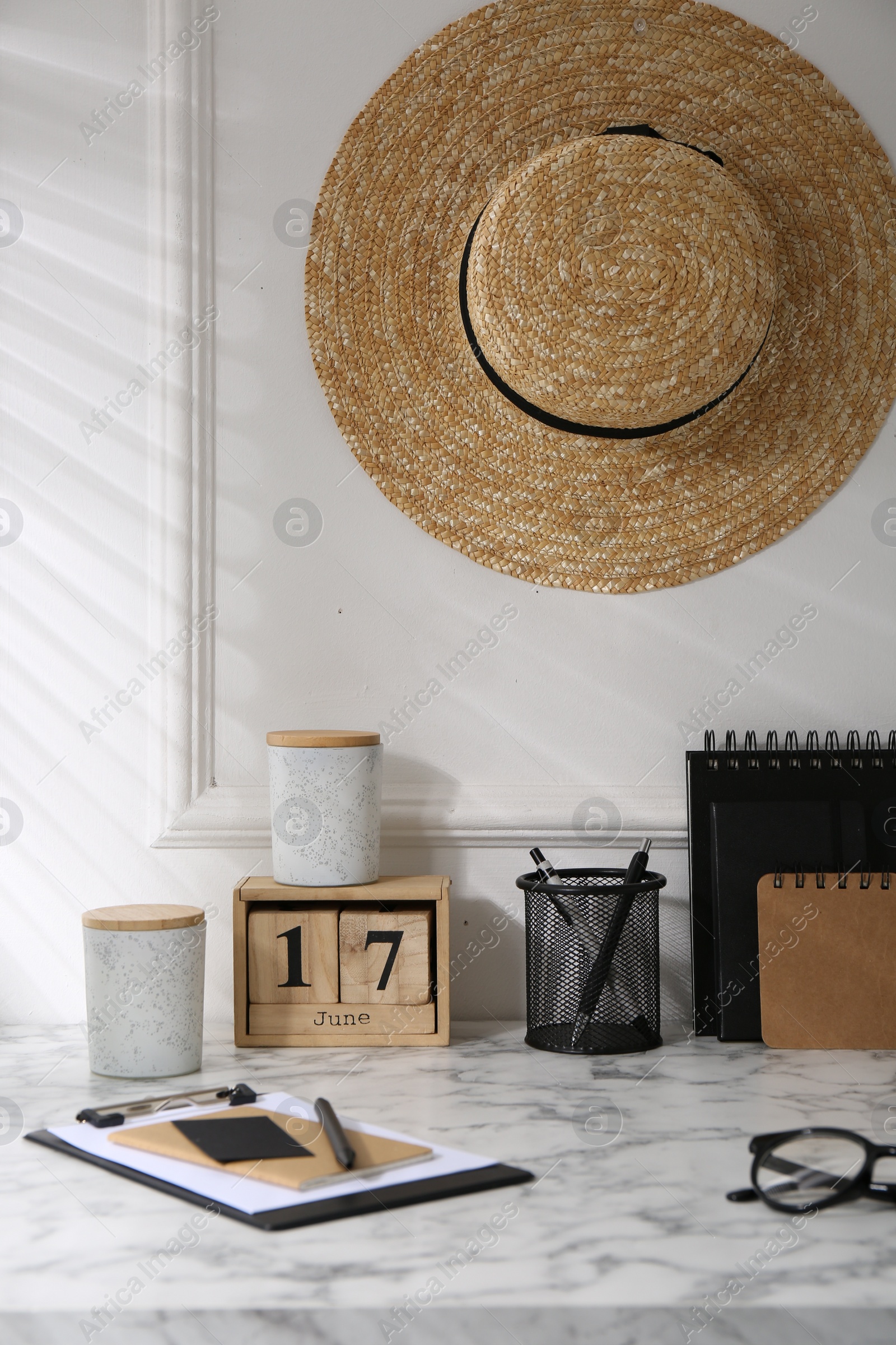 Photo of Stylish office workplace. Decor elements, glasses, cup and stationery on marble table near white wall