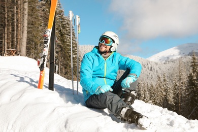 Photo of Man with ski equipment sitting on snow in mountains. Winter vacation