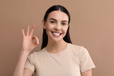 Photo of Beautiful woman with clean teeth smiling and showing OK gesture on beige background