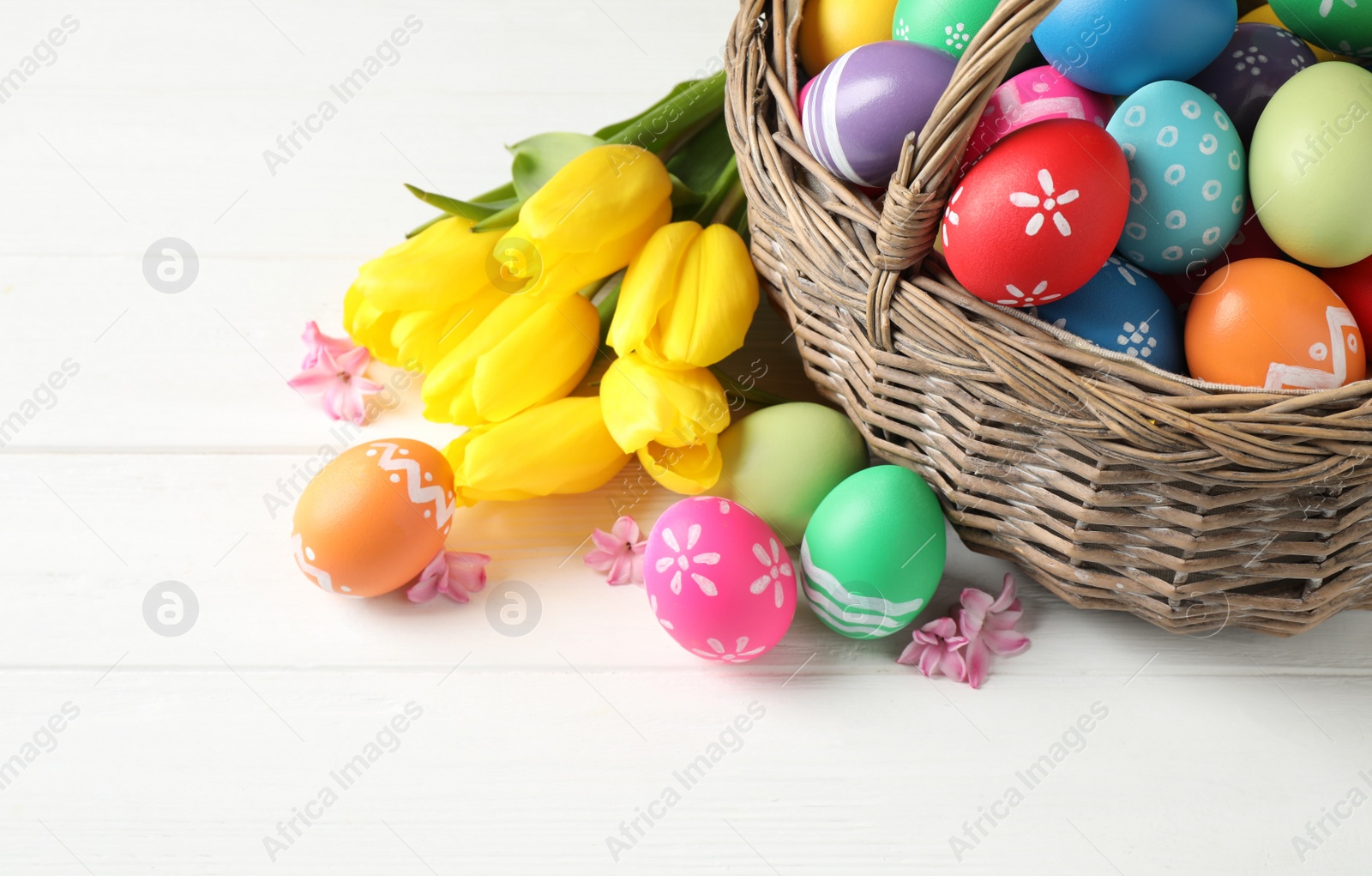 Photo of Colorful Easter eggs and flowers on white wooden background. Space for text