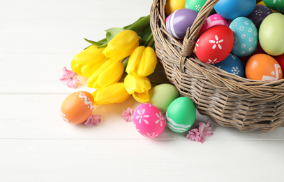 Photo of Colorful Easter eggs and flowers on white wooden background. Space for text