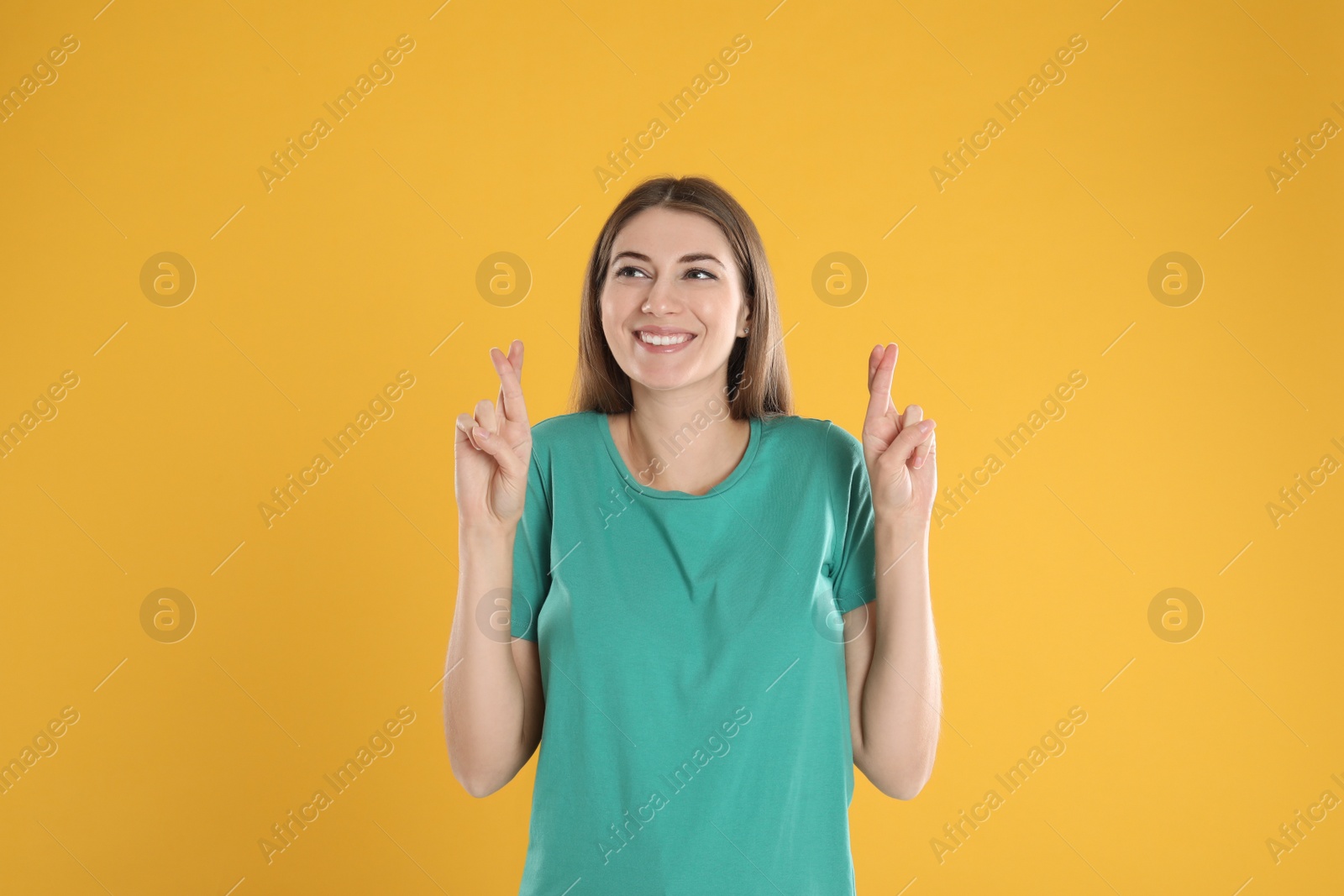 Photo of Woman with crossed fingers on yellow background. Superstition concept
