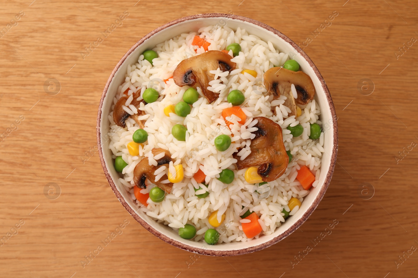 Photo of Bowl of delicious rice with vegetables on wooden table, top view