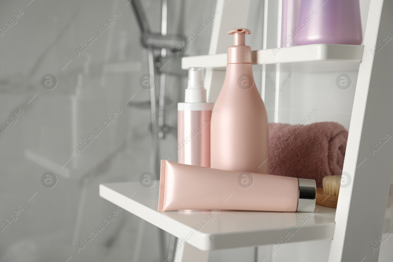 Photo of Different hair care products and towel on shelving unit in bathroom