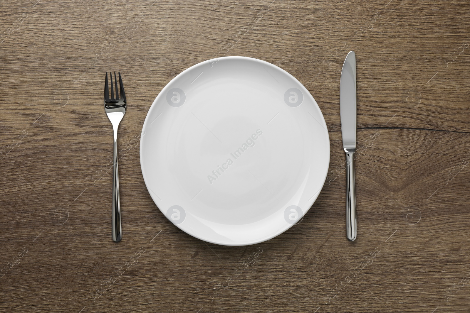 Photo of Empty plate, fork and knife on wooden table, top view