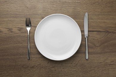 Photo of Empty plate, fork and knife on wooden table, top view