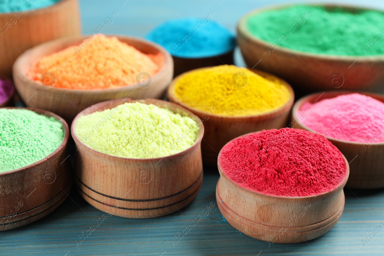 Photo of Colorful powder dyes on light blue wooden background, closeup. Holi festival