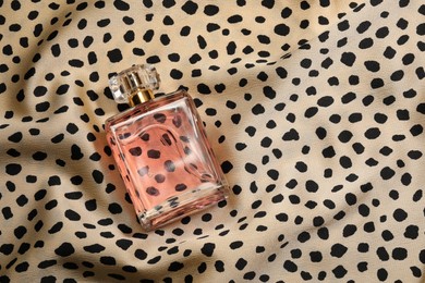 Photo of Luxury perfume in bottle on fabric with leopard pattern, top view