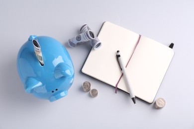 Photo of Financial savings. Piggy bank, dollar banknotes, coins and stationery on grey background, flat lay