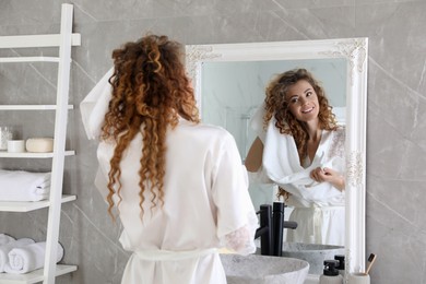 Photo of Beautiful woman drying hair with towel near mirror in bathroom