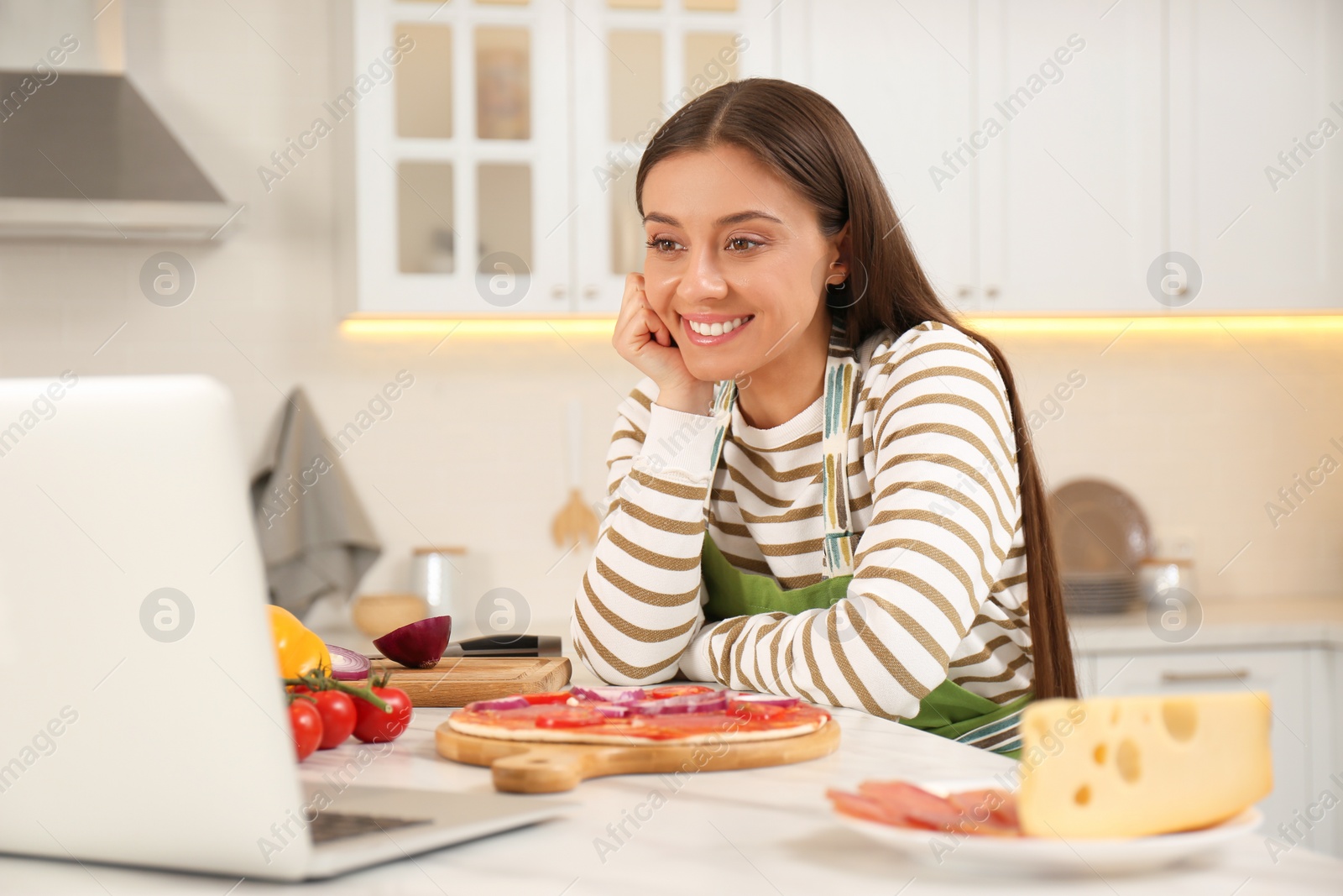 Photo of Happy woman watching online cooking course via laptop in kitchen
