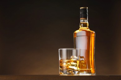 Whiskey with ice cubes in glass and bottle on table, space for text