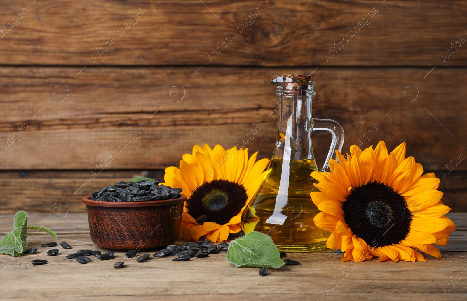 Photo of Sunflower cooking oil, seeds and yellow flowers on wooden table