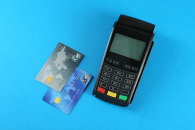 New modern payment terminal and credit cards on light blue background, flat lay