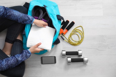 Photo of Young woman packing sports bag on floor, top view