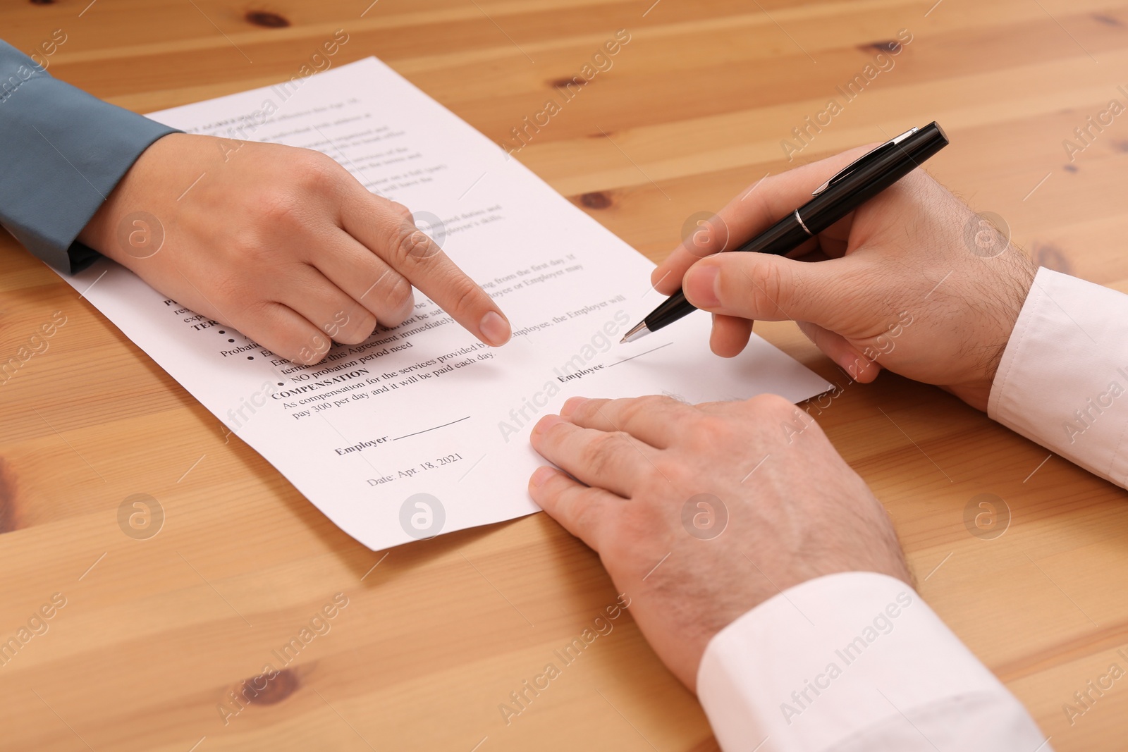 Photo of Businesspeople signing contract at wooden table, closeup of hands