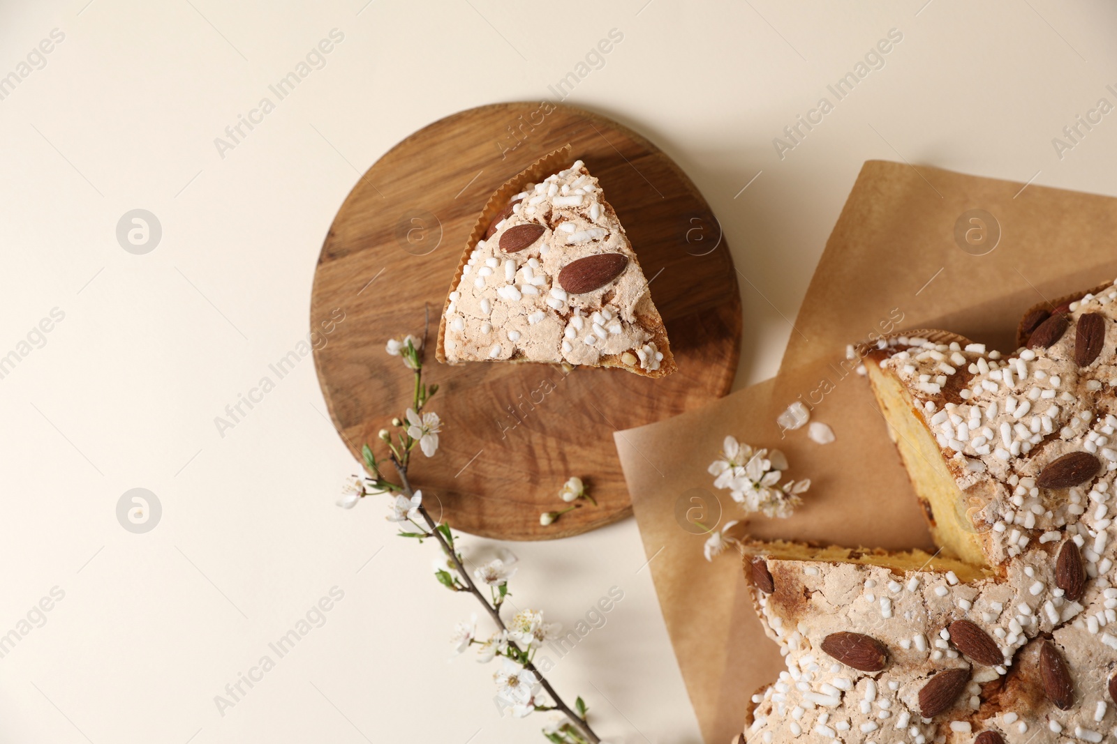 Photo of Delicious cut Italian Easter dove cake (traditional Colomba di Pasqua) and flowering branch on beige table, flat lay. Space for text