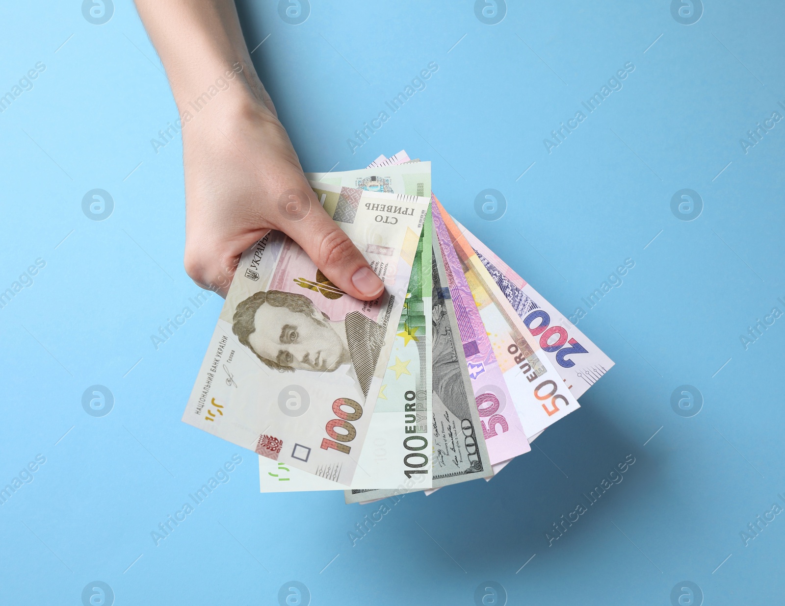 Image of Currency exchange. Woman holding euro, hryvnia and dollar banknotes on light blue background, closeup