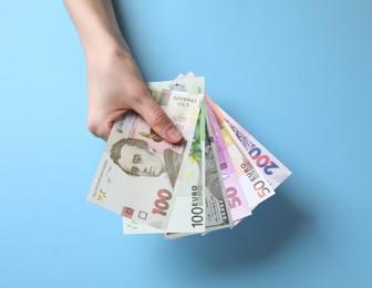 Image of Currency exchange. Woman holding euro, hryvnia and dollar banknotes on light blue background, closeup