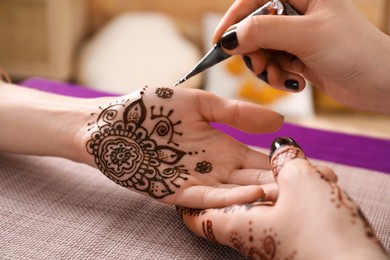 Photo of Professional mehndi master making henna tattoo indoors, closeup