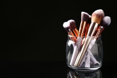 Photo of Jar of makeup brushes on dark background. Space for text