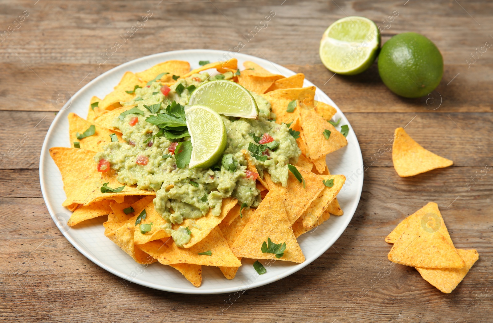 Photo of Plate of delicious mexican nachos chips with guacamole sauce and lime on wooden table