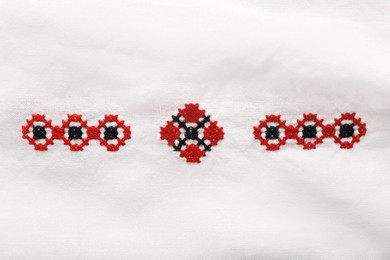 Photo of Beautiful red Ukrainian national embroidery on white fabric, top view