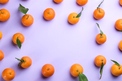 Fresh ripe tangerines with green leaves on lilac background, flat lay. Space for text