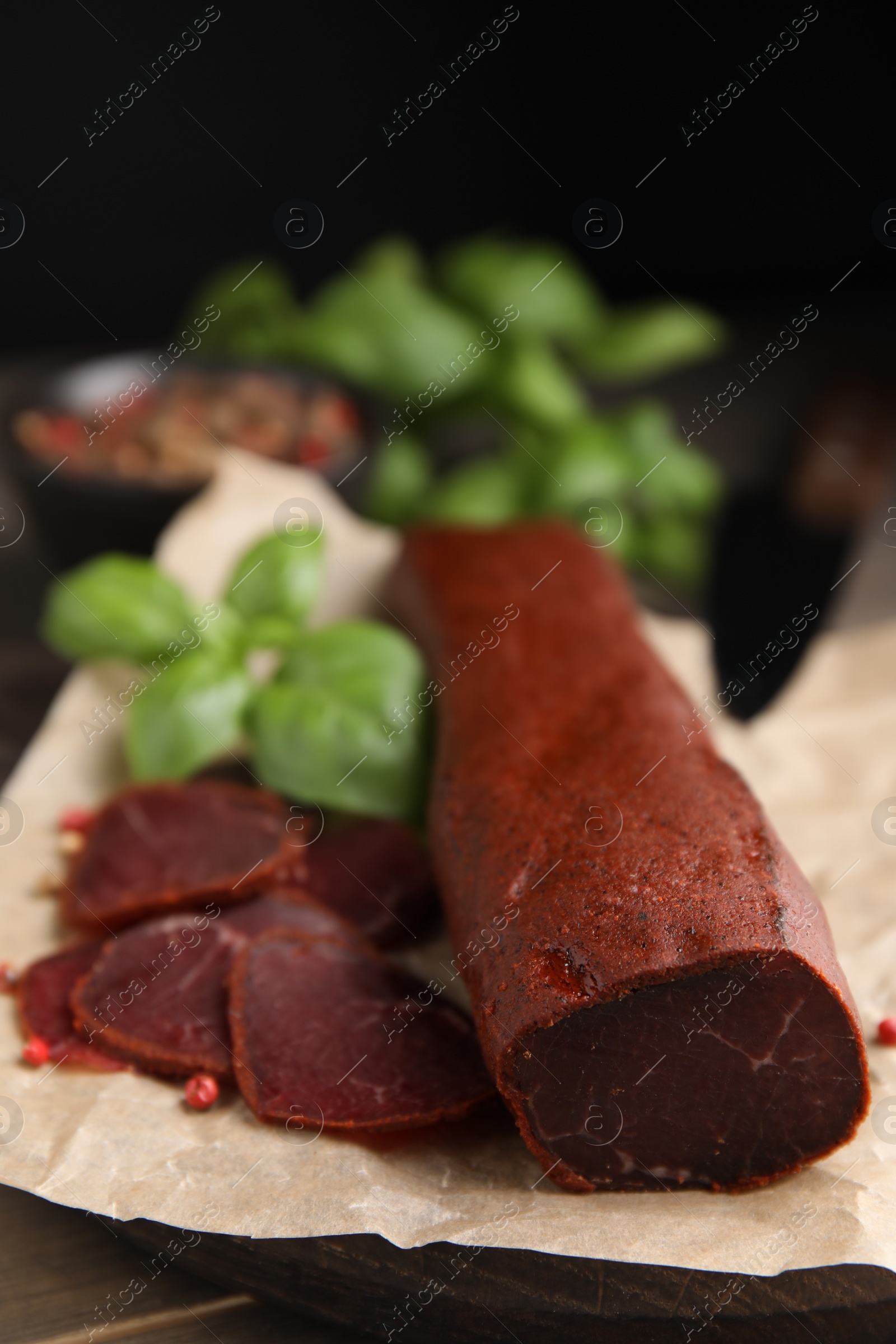 Photo of Delicious dry-cured beef basturma with basil and peppercorns on wooden table, closeup