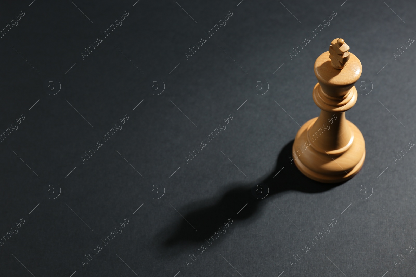 Photo of White wooden chess king on dark background, above view. Space for text