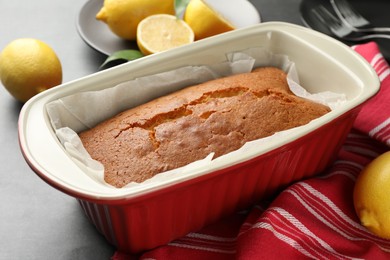 Photo of Tasty lemon cake in baking dish and citrus fruits on grey table, closeup