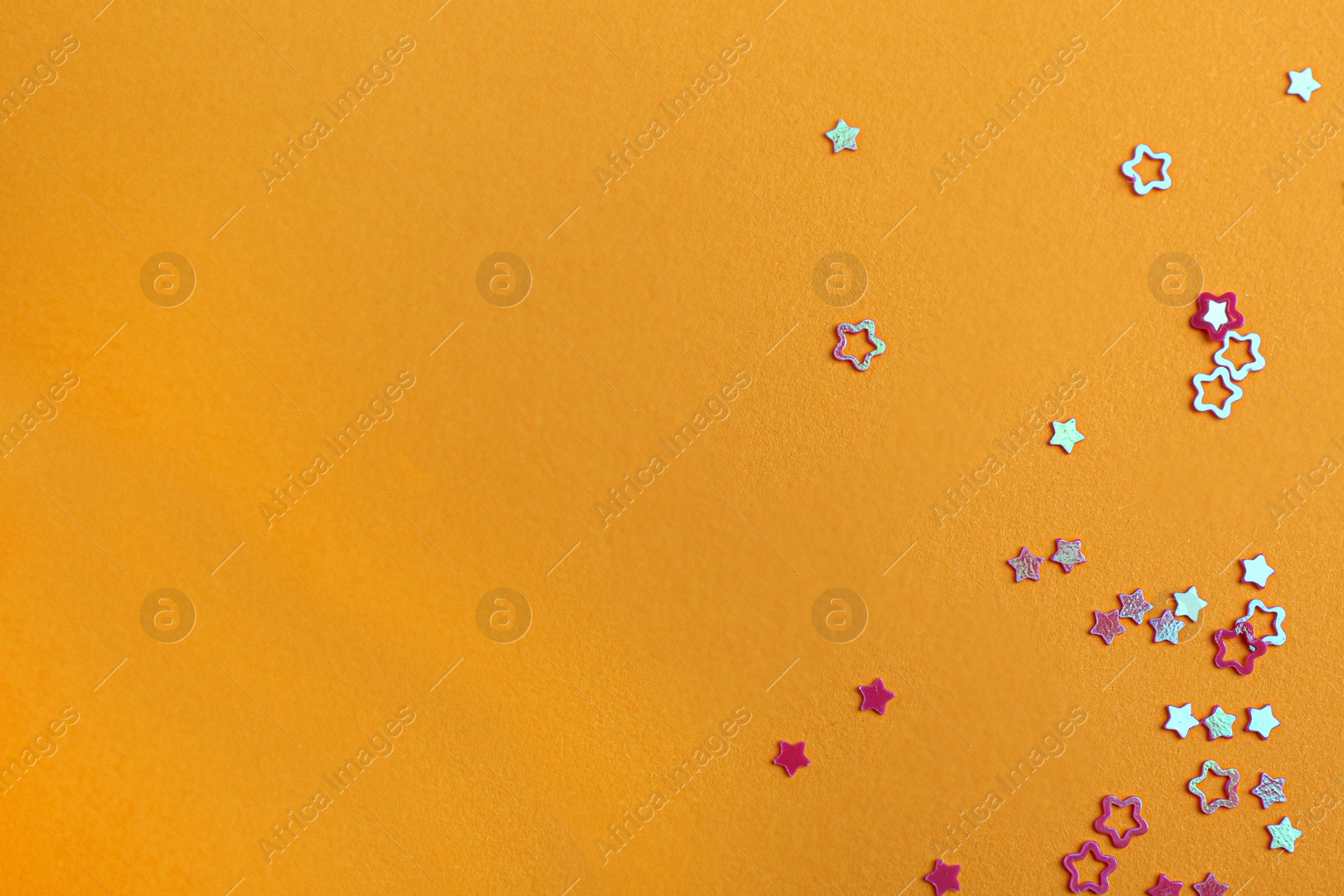 Photo of Shiny bright star shaped glitter on pale orange background. Space for text