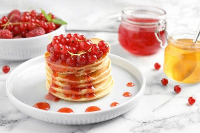 Delicious pancakes with fresh berries and syrup on marble table