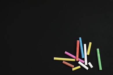 Photo of Colorful chalks on black board, flat lay. Space for text