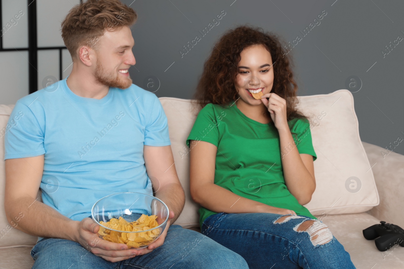 Photo of Young couple with snack and video game controller on sofa indoors