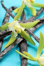 Photo of Vanilla pods and beautiful flowers on light blue background, closeup