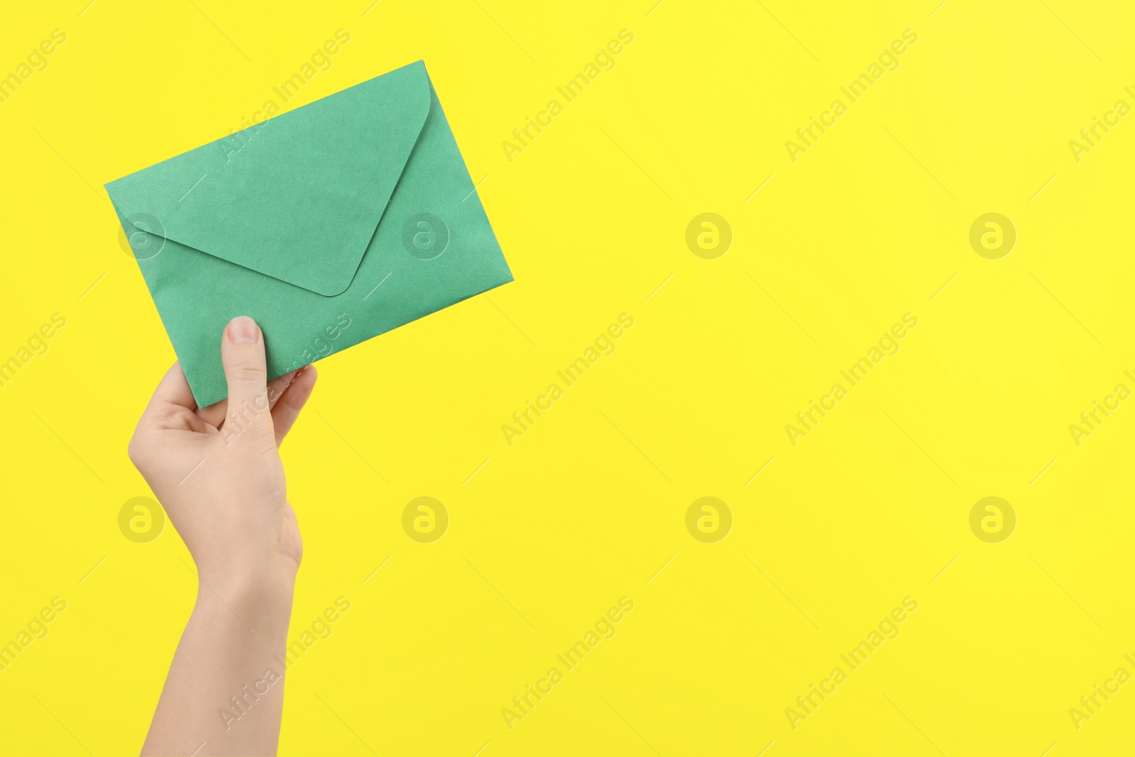 Photo of Woman holding green paper envelope on yellow background, closeup. Space for text