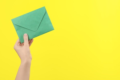 Woman holding green paper envelope on yellow background, closeup. Space for text