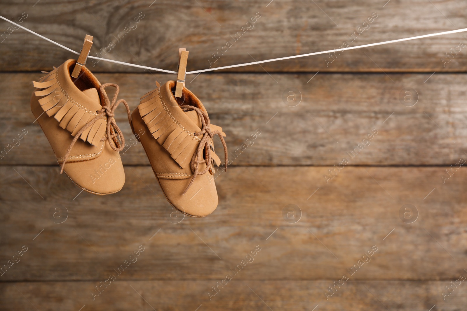 Photo of Pair of shoes on laundry line against wooden background, space for text. Baby accessories