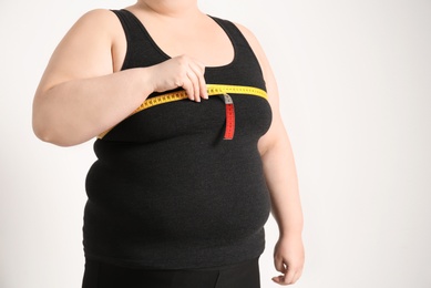 Overweight woman with measuring tape on light background