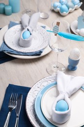Photo of Festive table setting with bunny ears made of light blue eggs and napkins. Easter celebration