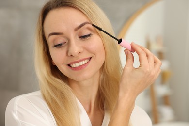 Beautiful woman applying mascara with brush indoors